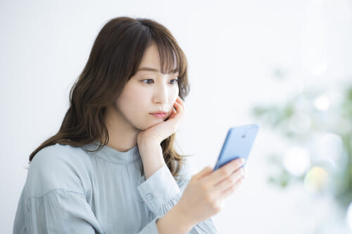 スマホ画面を見ながら考える女性